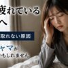朝から疲れている女性がベッドに座り、寝ても疲れが取れない原因について悩んでいる様子。睡眠環境やパジャマ選びの重要性を解説するイメージ画像